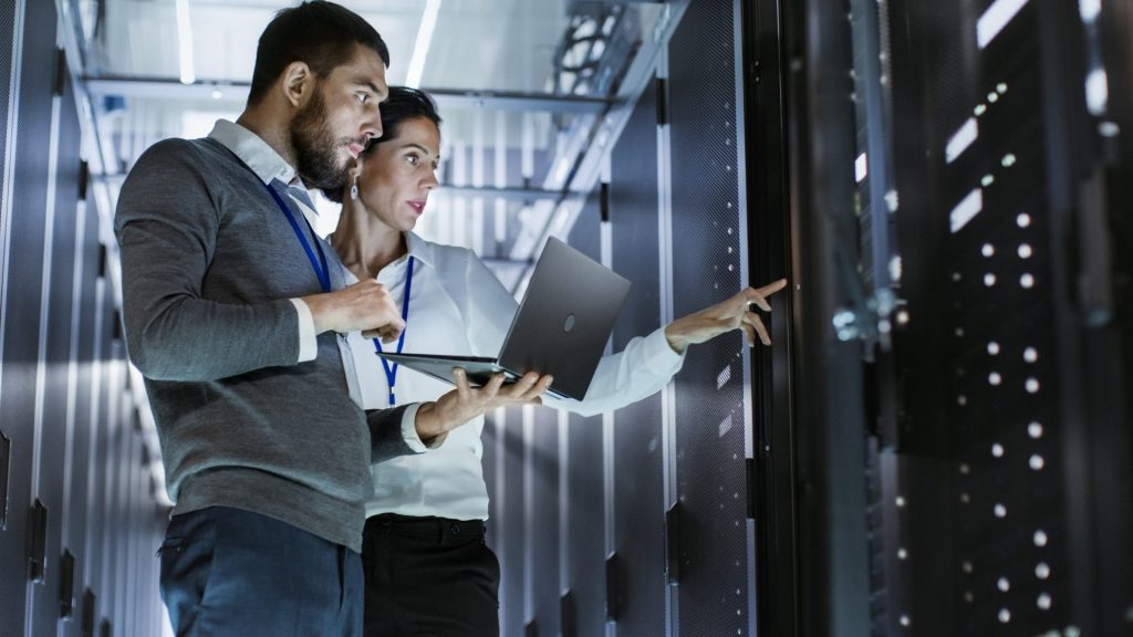 A man and woman with a laptop looking over server racks in a data center